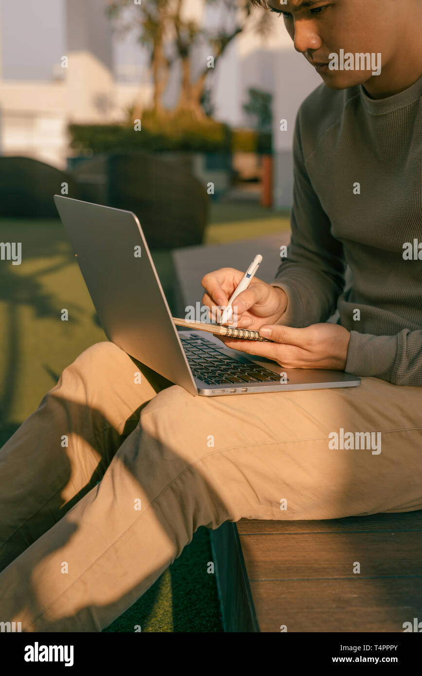 Un homme assis à l'ordinateur portable sur ses genoux et l'écriture de l'ordinateur portable Banque D'Images
