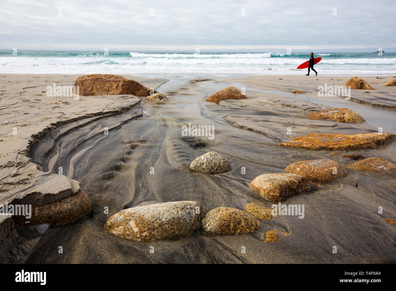 Blocs de granite dans Sennen, Cornwall, UK avec un homme portant une planche de surf. Banque D'Images