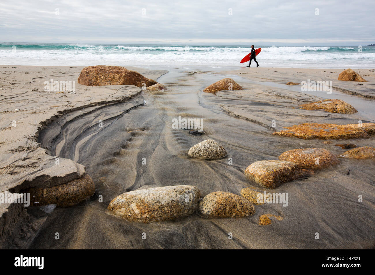Blocs de granite dans Sennen, Cornwall, UK avec un homme portant une planche de surf. Banque D'Images