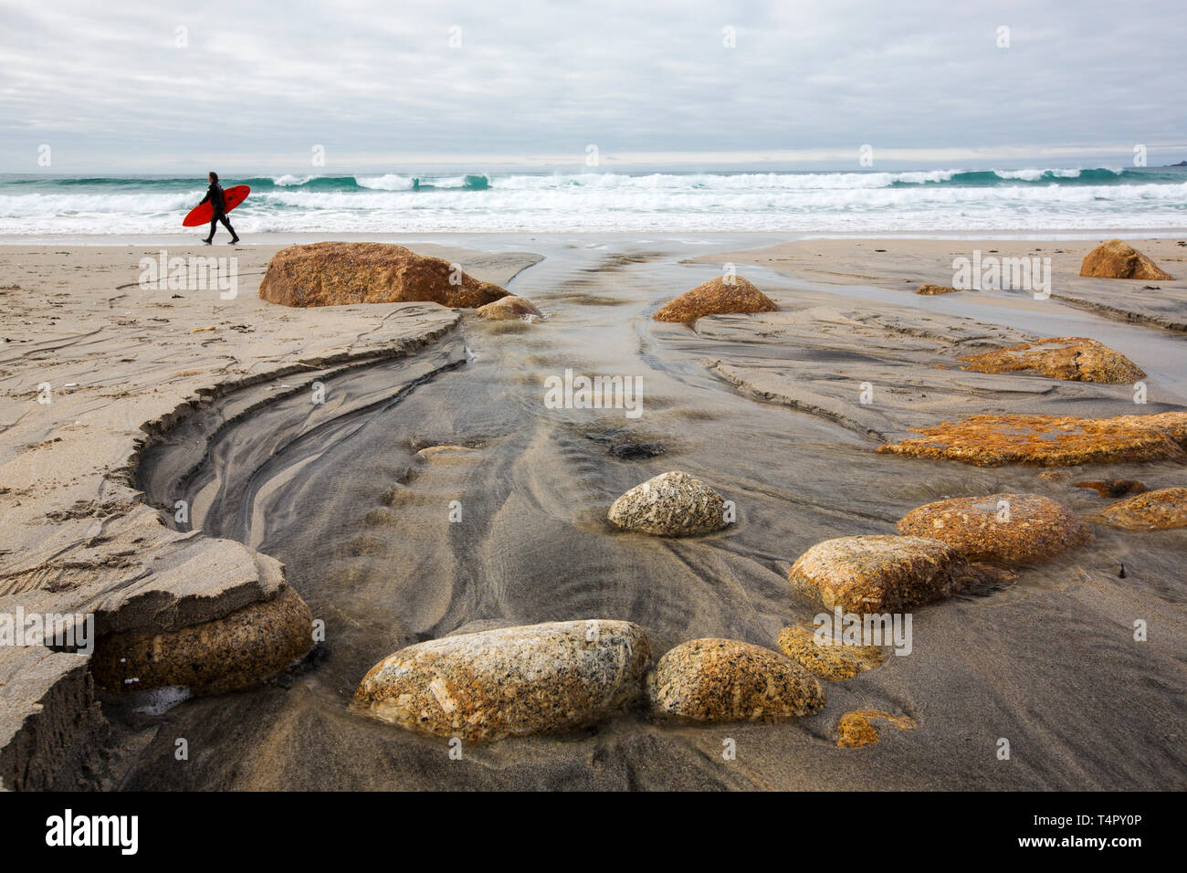 Blocs de granite dans Sennen, Cornwall, UK avec un homme portant une planche de surf. Banque D'Images