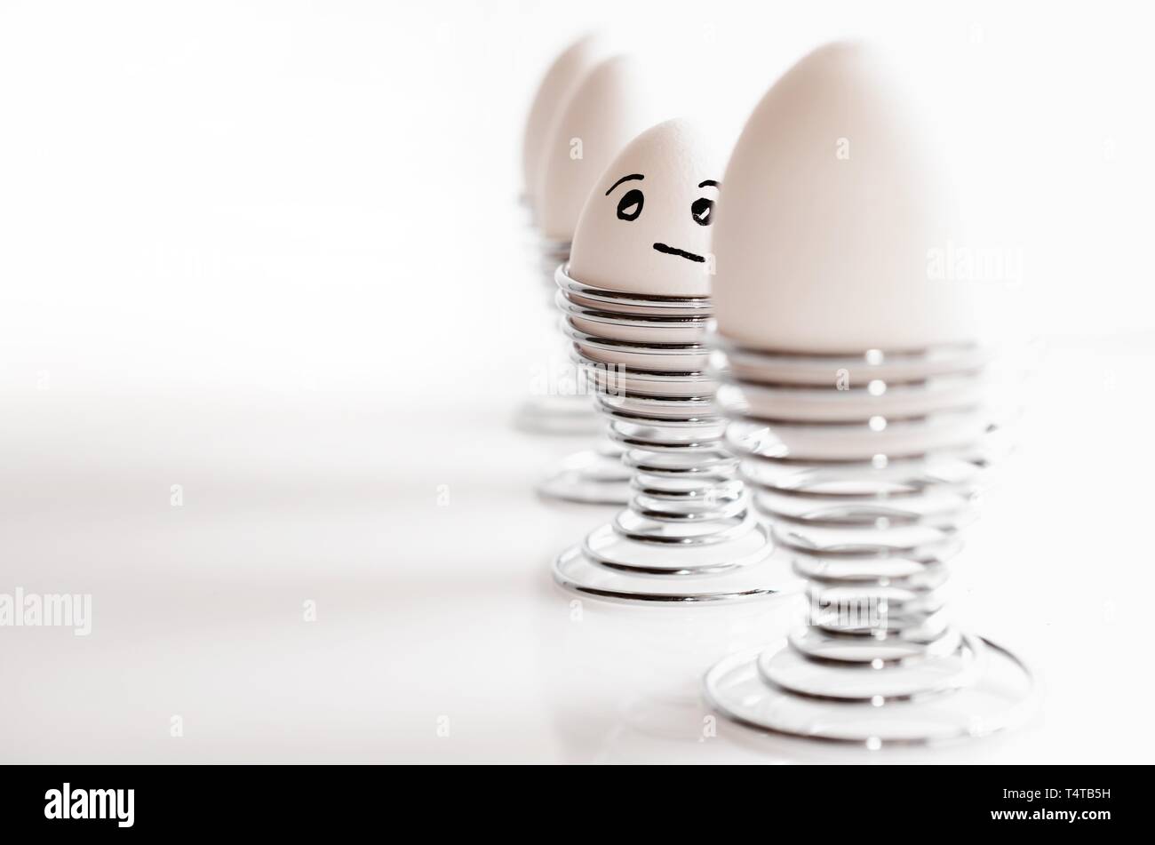 Une ligne de quatre œufs de poule blanche en argent cm, l'un avec l'expression du visage. Banque D'Images