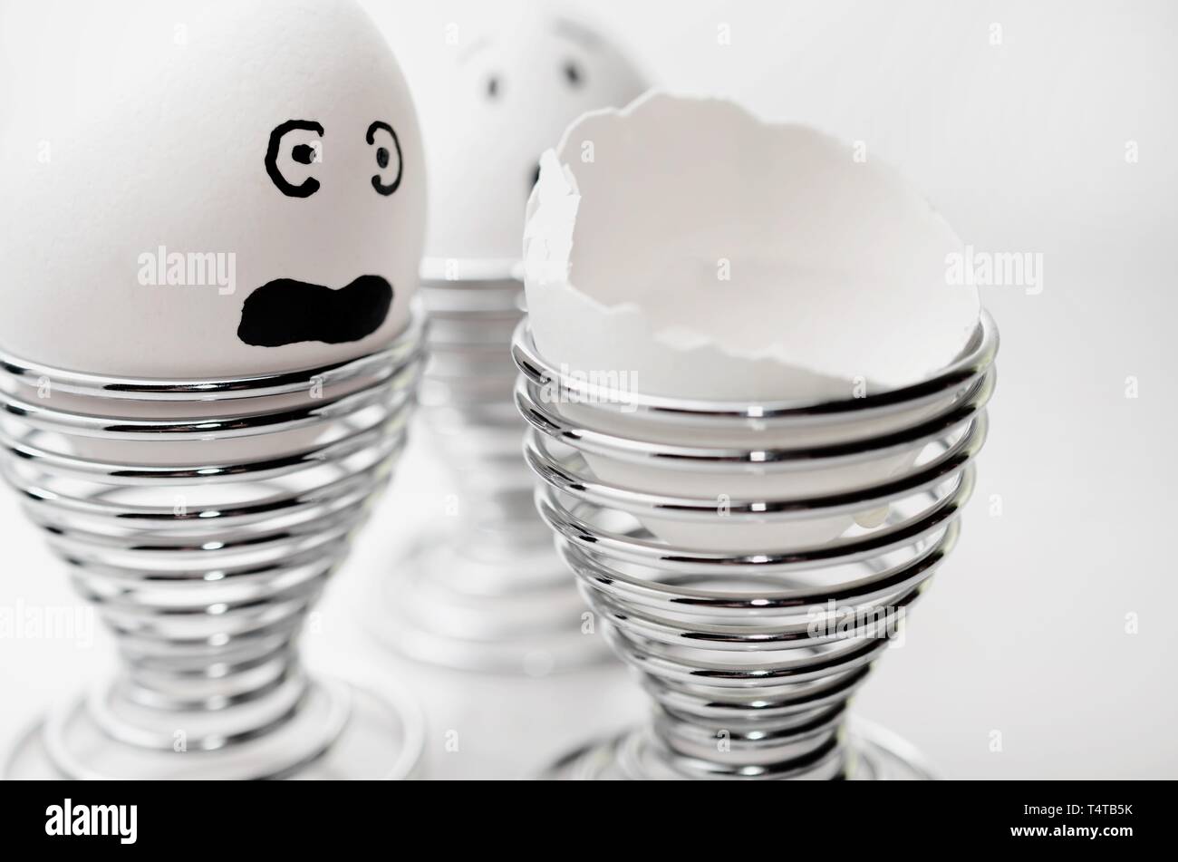 Trois œufs de poulet anthropomorphe en silver egg cups, un oeuf cassé. Banque D'Images