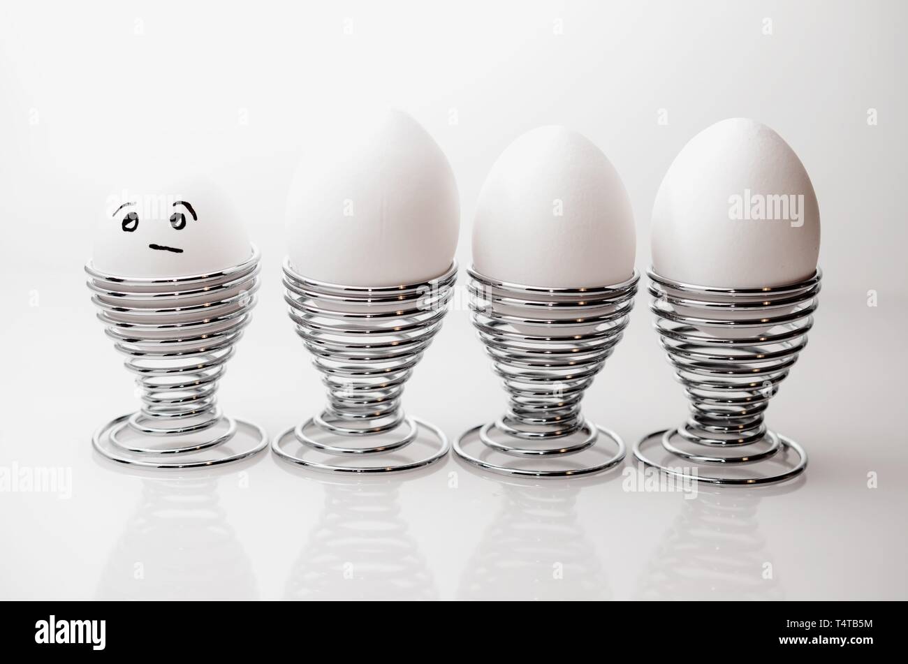 Quatre œufs de poule blanche en argent cm, un oeuf de poule anthropomorphe avec expression du visage, le grincheux à silver egg cups. Banque D'Images