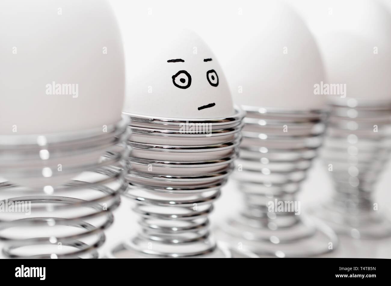 Quatre œufs de poule blanche en argent cm, un oeuf de poule anthropomorphe avec expression du visage, le grincheux à silver egg cups. Banque D'Images