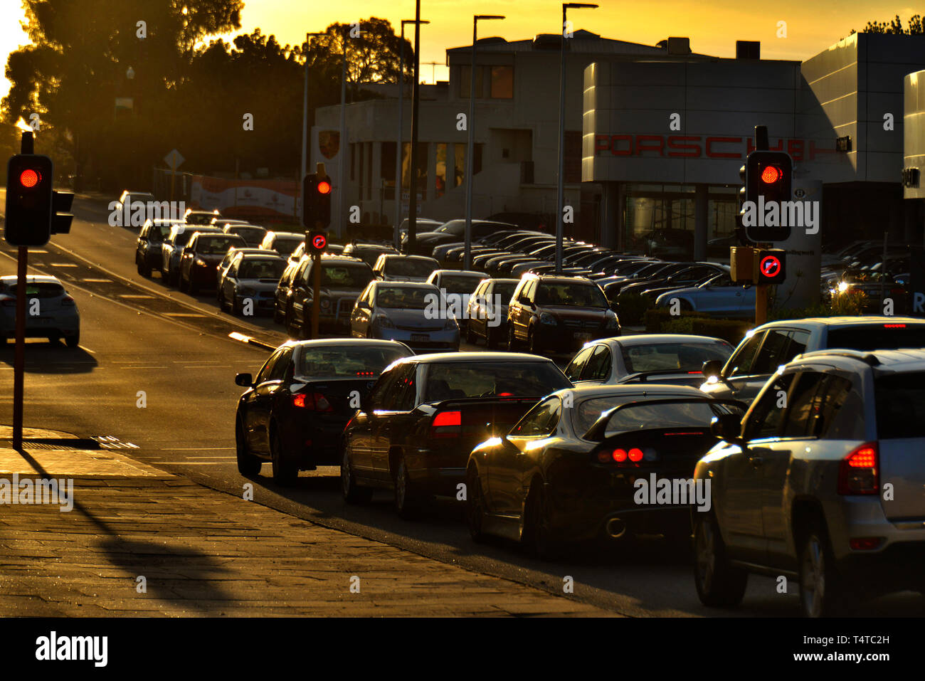 Une longue rue de banlieue, avec des voitures pare-chocs à pare-chocs, aux feux en attendant de se déplacer. Par contre-jour coucher du soleil. L'ouest de l'Australie. Banque D'Images