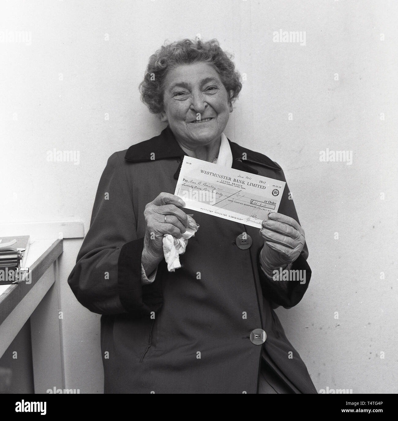 1967, historiques, 'spot' la balle, une dame âgée nous tend un chèque bancaire de Westminster €25.00 pour gagner un journal local de la concurrence, England, UK. Banque D'Images