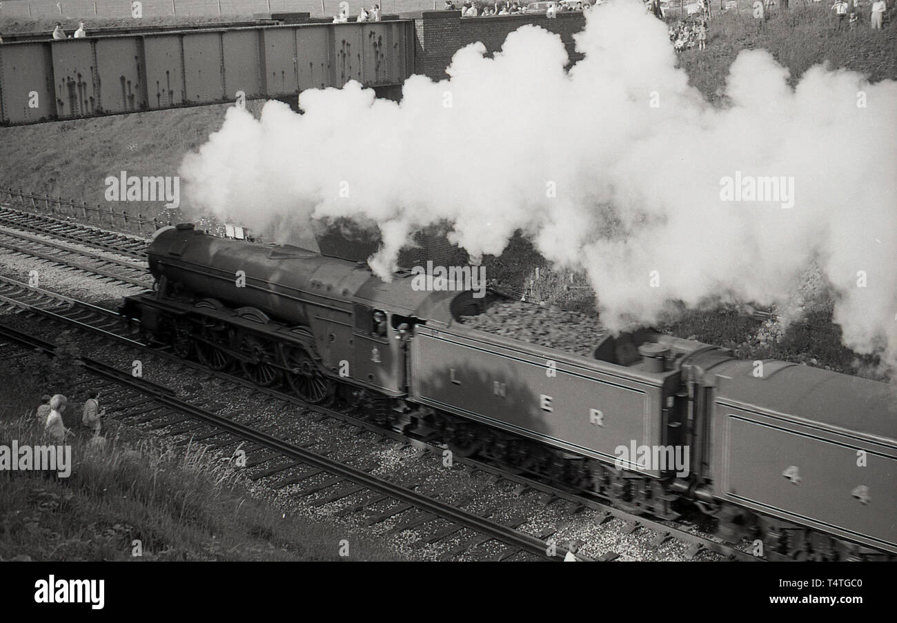 1969, historique, sur un pont et une grassbank, regarder les gens comme la célèbre locomotive à vapeur, le Flying Scotsman', va passé, England, UK. Banque D'Images