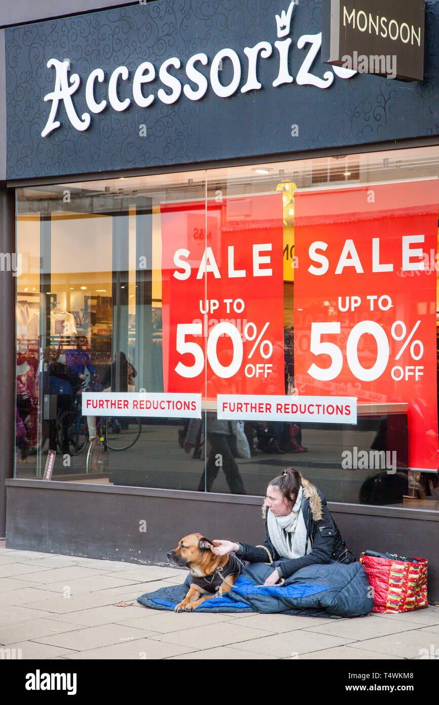 Femme sans-abri mendiant avec chien assis à l'extérieur de la boutique Accessorize à Cheltenham mendier au large de consommateurs et des passants au cours de la vente Janvier Banque D'Images