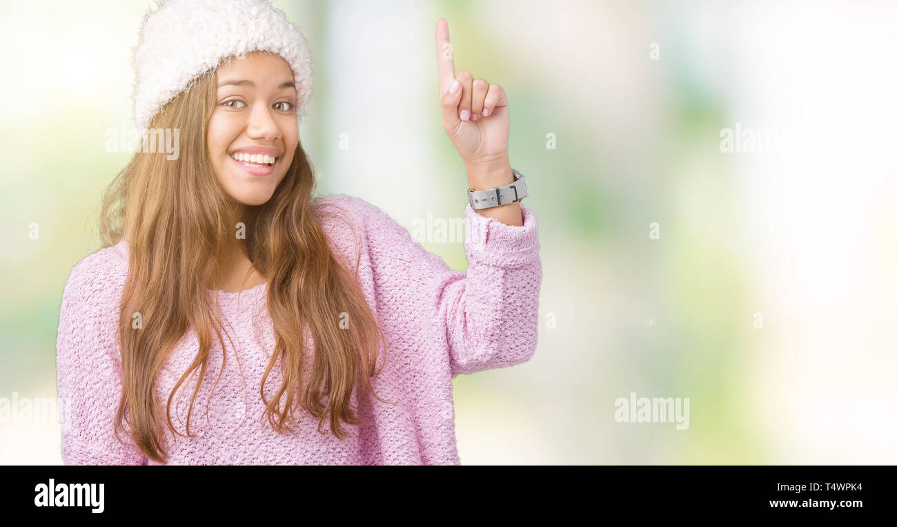 Jeune belle brunette woman wearing sweater et chapeau d'hiver sur fond isolé montre de l'index jusqu'à une bonne idée. Quitté et heureux. Numb Banque D'Images
