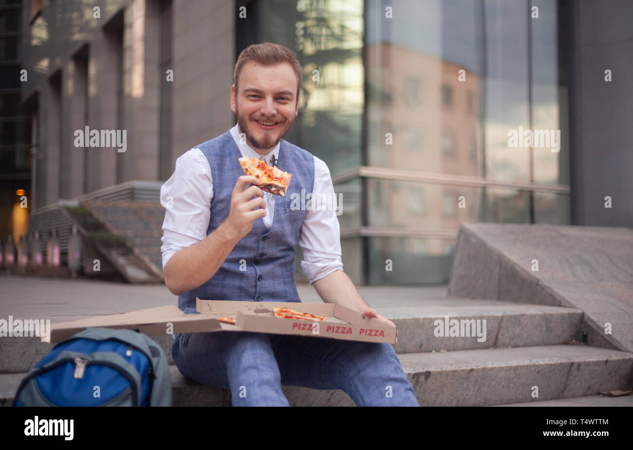 Un jeune homme, 29 ans, manger une pizza slice, à la recherche d'appareil photo. Banque D'Images