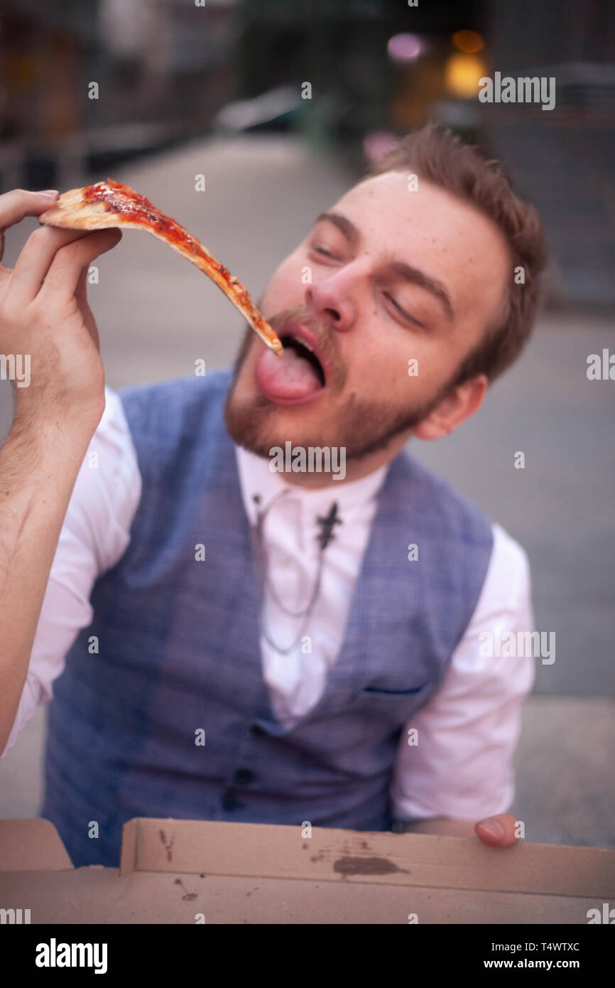 Un jeune homme, 29 ans, de manger sa dernière coupe pizza, vue de face. Banque D'Images