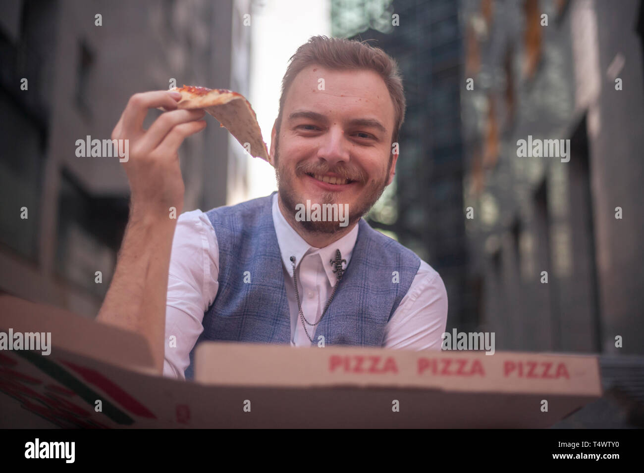 Un jeune homme, 29 ans, tenant une tranche de pizza, à la recherche d'appareil photo. Banque D'Images