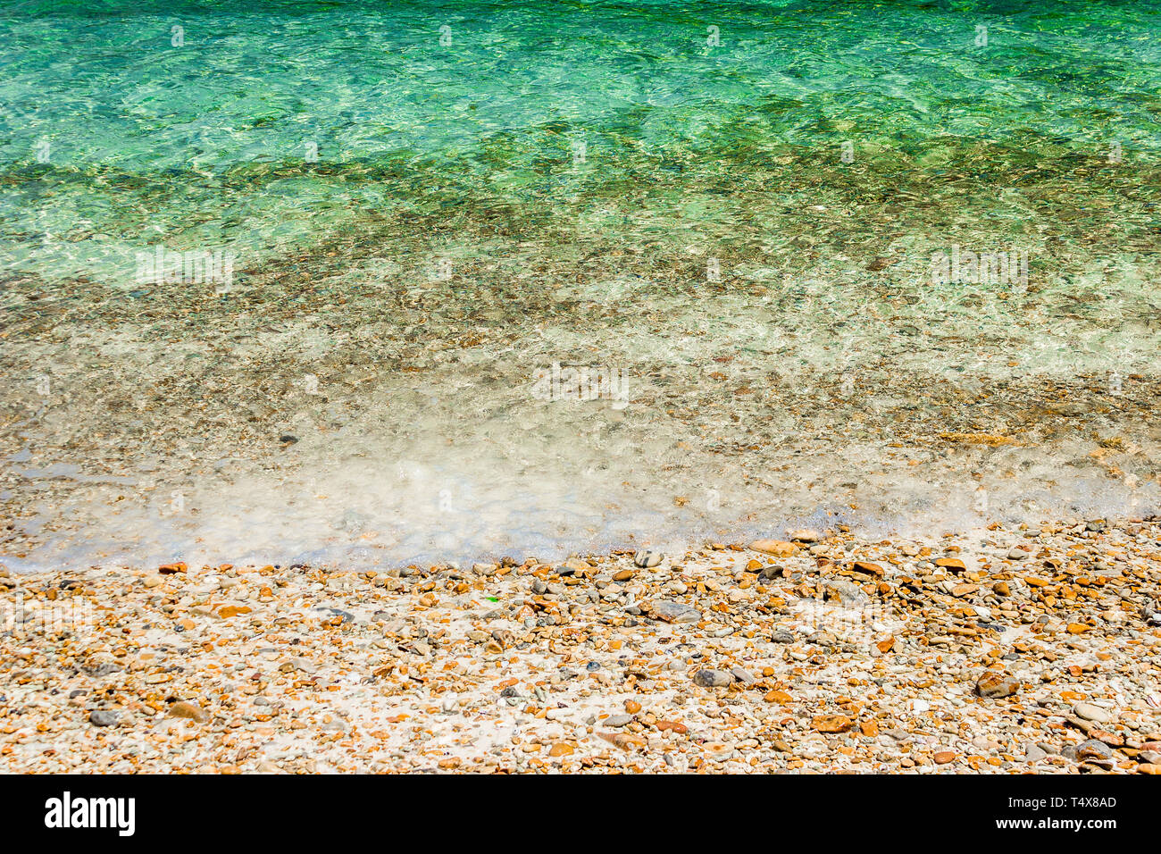 Vagues douces avec de la mousse d'eau sur les cailloux et plage de sable. Banque D'Images