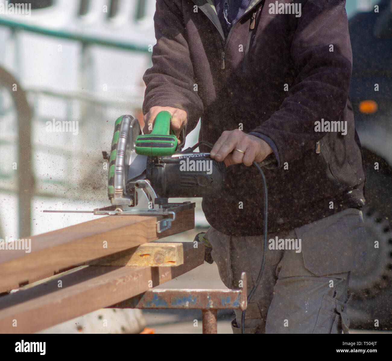 Menuisier charpentier de couper une planche de bois de teck avec une scie circulaire électrique Hitachi Banque D'Images