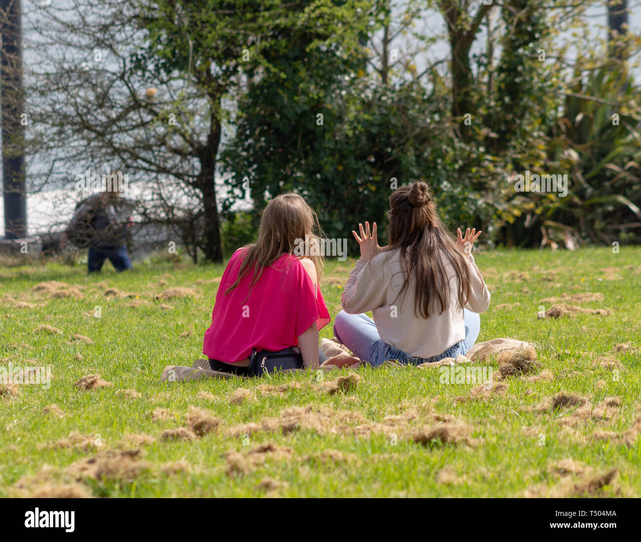 2 jeunes femmes filles s'assit sur l'herbe dans un parc, profitant du soleil. Banque D'Images