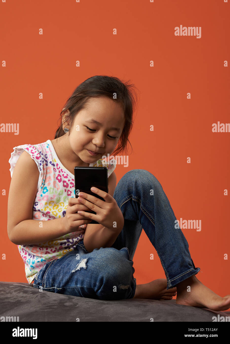 Asian girl Playing with téléphone sur un pouf poire et une couleur de fond. Banque D'Images