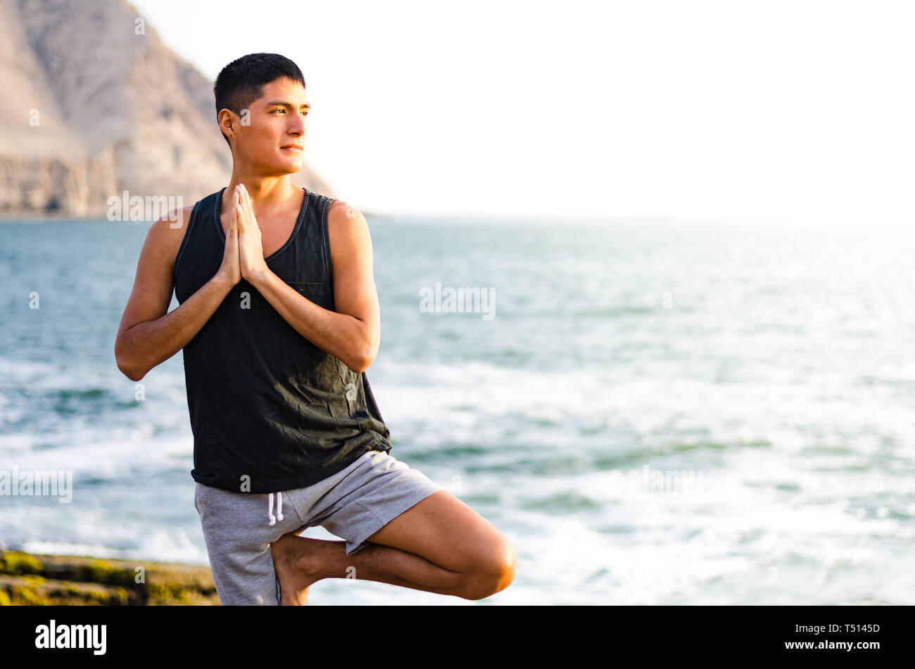 Jeune homme faisant du yoga et la méditation en position de l'arbre en mer plage. Vrikshasana Banque D'Images
