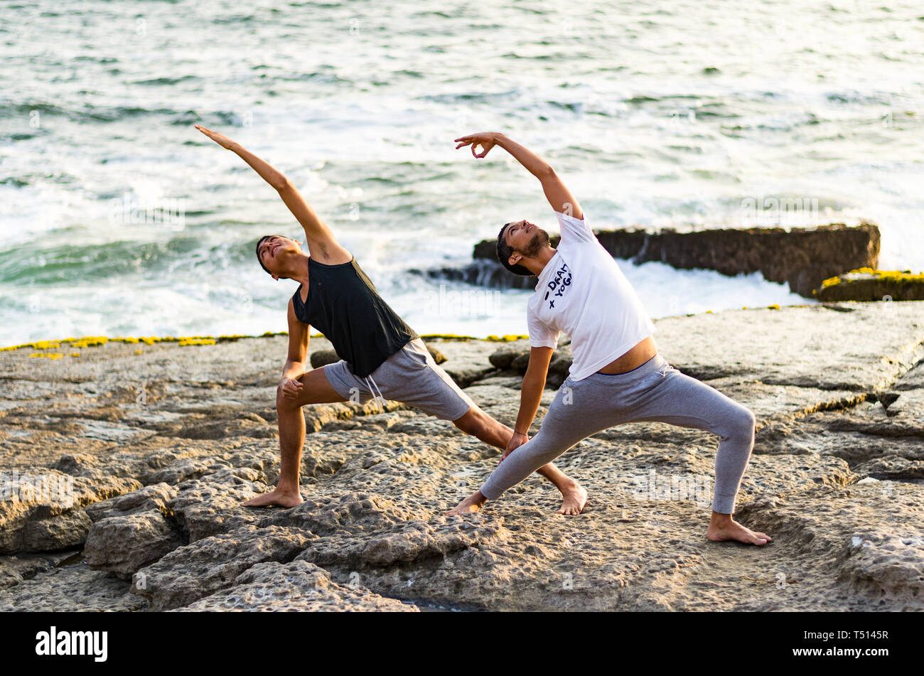 Les jeunes hommes sur la pratique des asanas de yoga d'été bilan session sur une belle plage d'or de Lima - Pérou sur un tour de yoga, Fulhadhoo, angle de côté Poser Utthita Parsvakonasana Banque D'Images