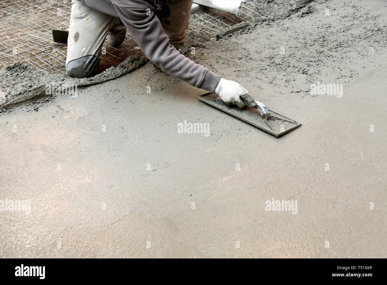 Travailleur de la construction à genoux avec mortier de ciment d'aplatissement d'une spatule à la main tout en faisant un sol en béton Banque D'Images
