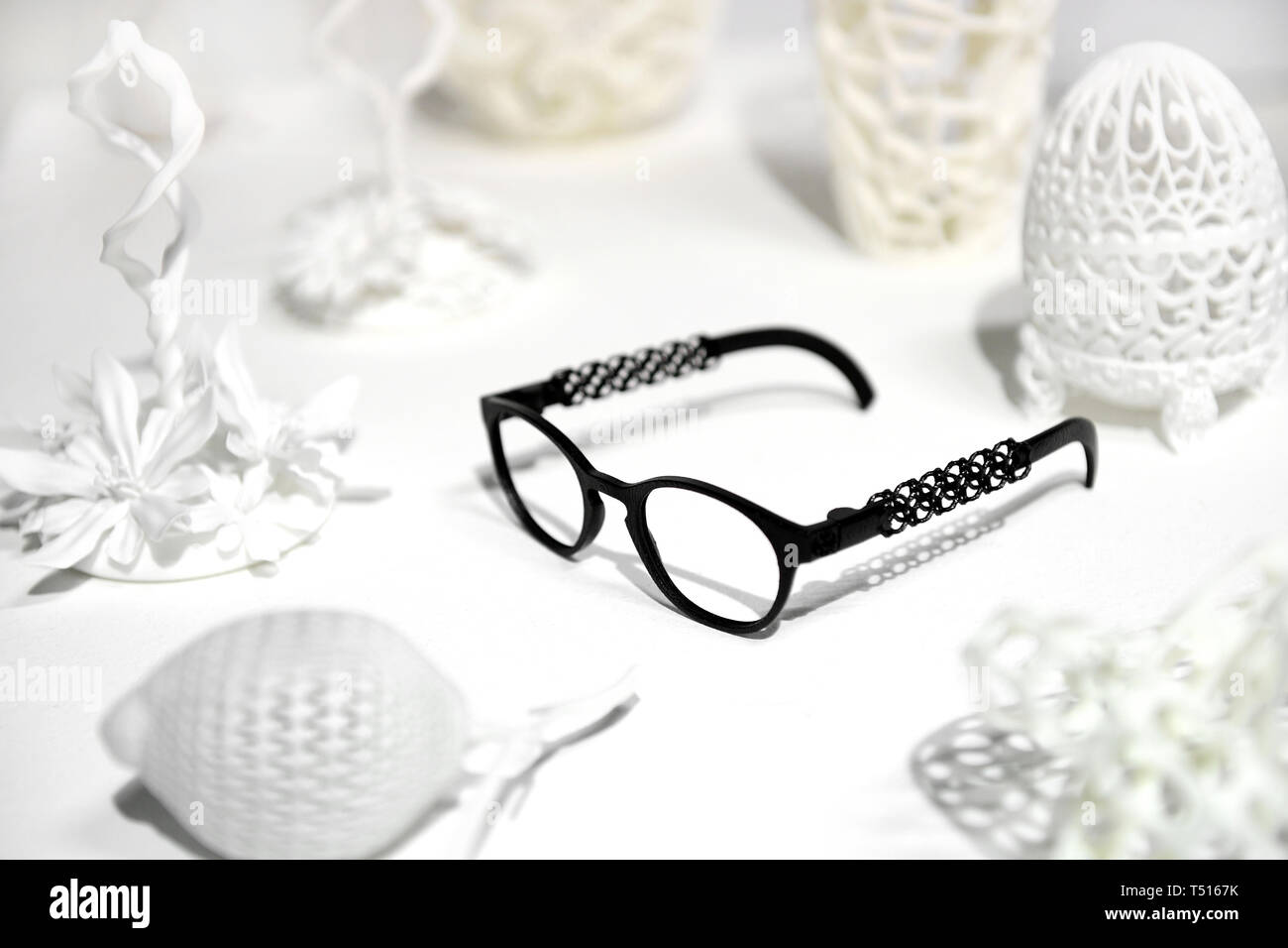 Lunettes 3D noir imprimé blanc parmi les formes complexes avec des échantillons de l'objet imprimante 3D, assis sur la surface blanche Banque D'Images