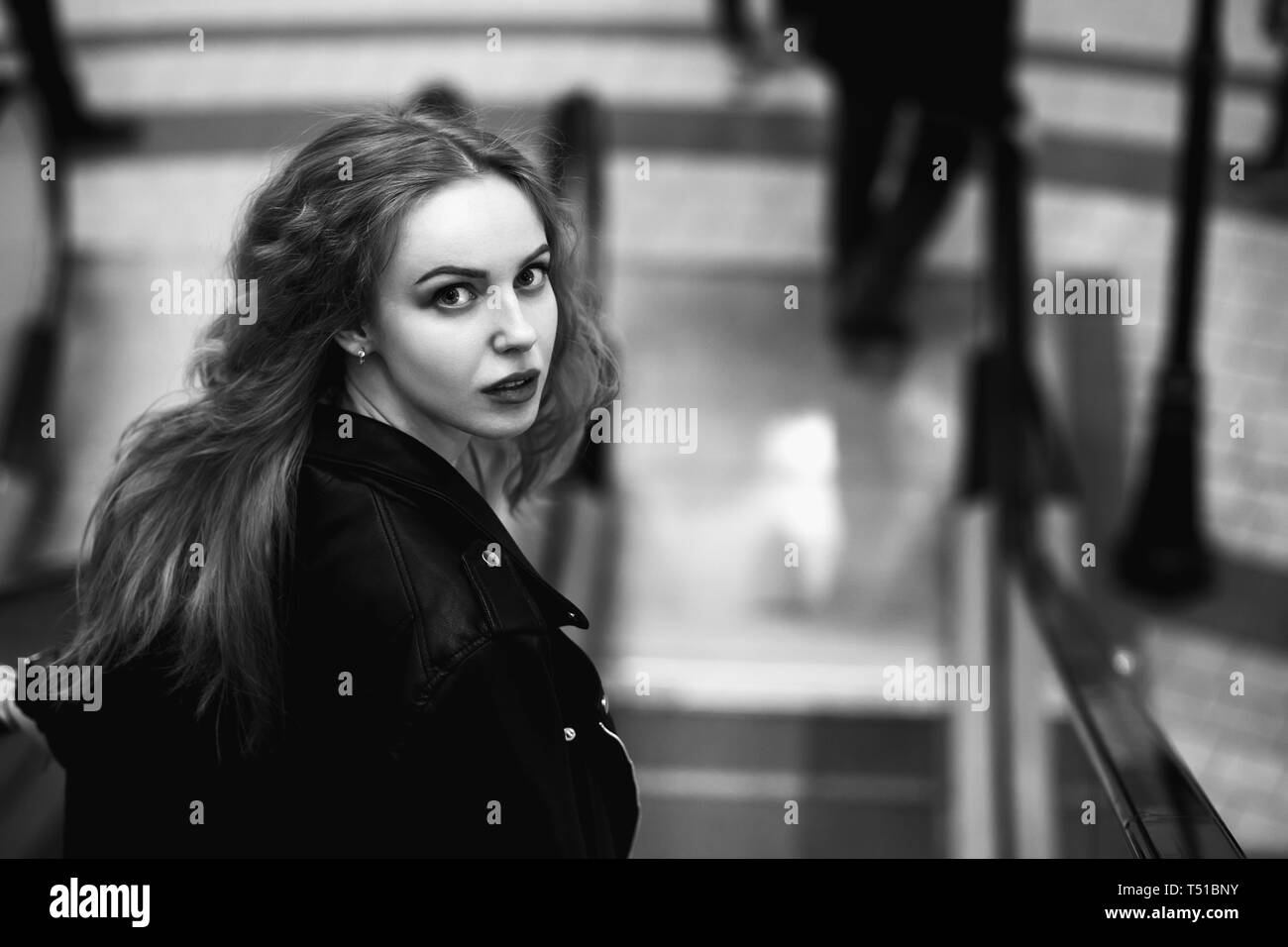 Peur belle blonde curly jeune femme à l'arrière, debout sur l'escalator, monochrome Banque D'Images