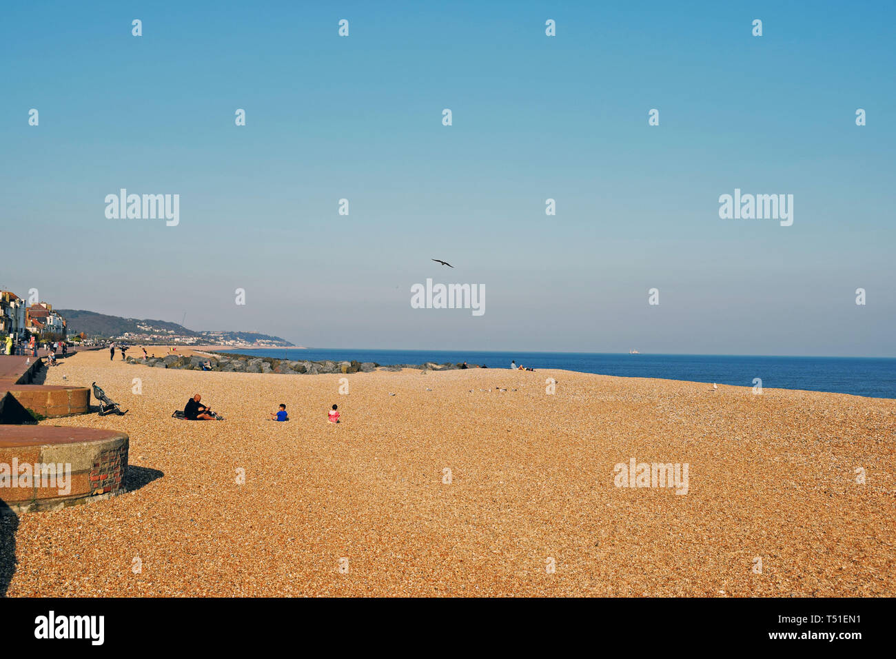Une scène de bord de mer de personnes s'amusant sur la plage de galets dans le Kent en Angleterre avec un fond de ciel bleu Banque D'Images