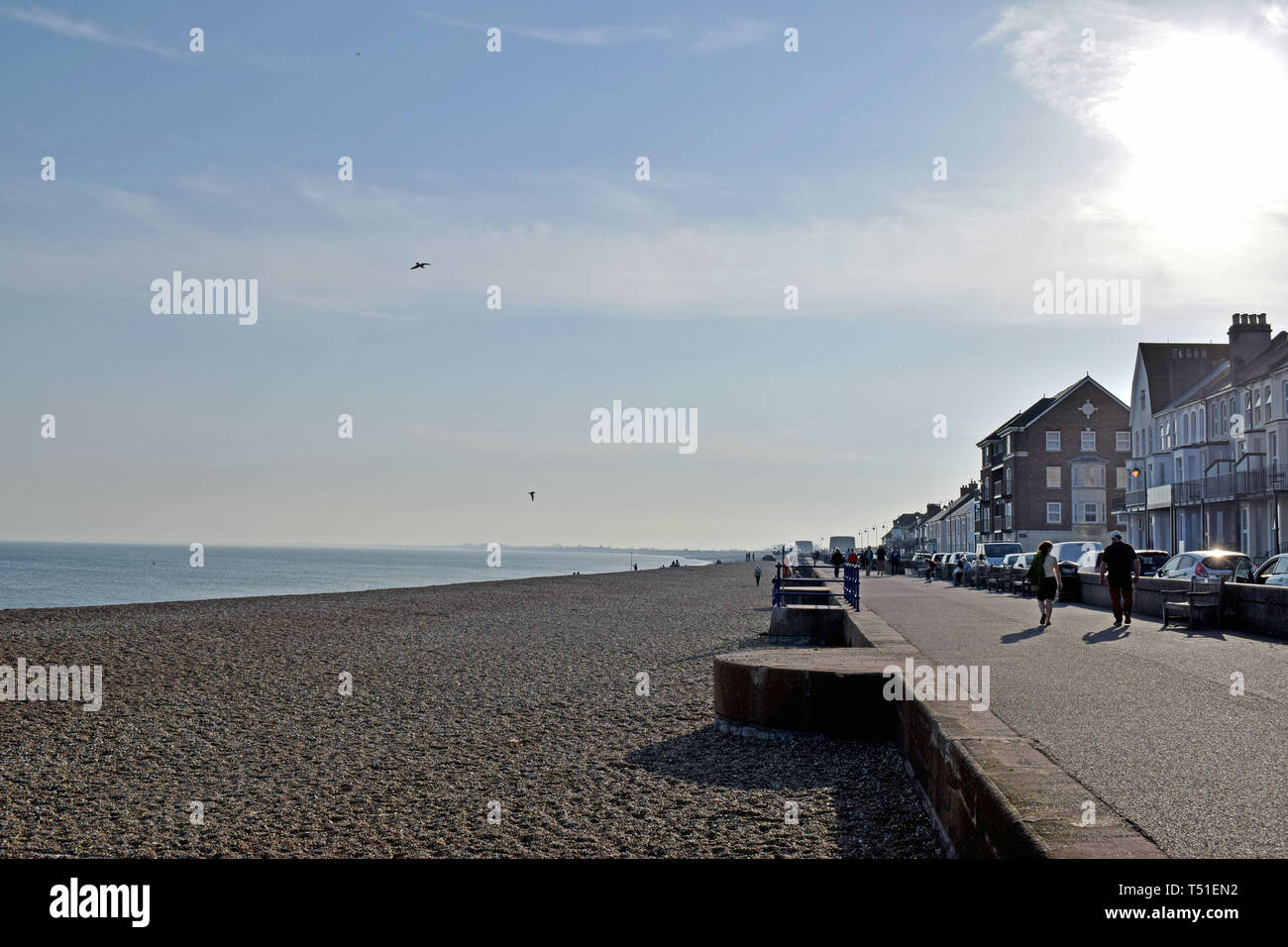 Une scène de bord de mer dans le Kent en Angleterre, les gens qui marchent le long du front de mer avec des maisons d'un côté et la plage de galets et de la mer et ciel bleu l'autre côté Banque D'Images