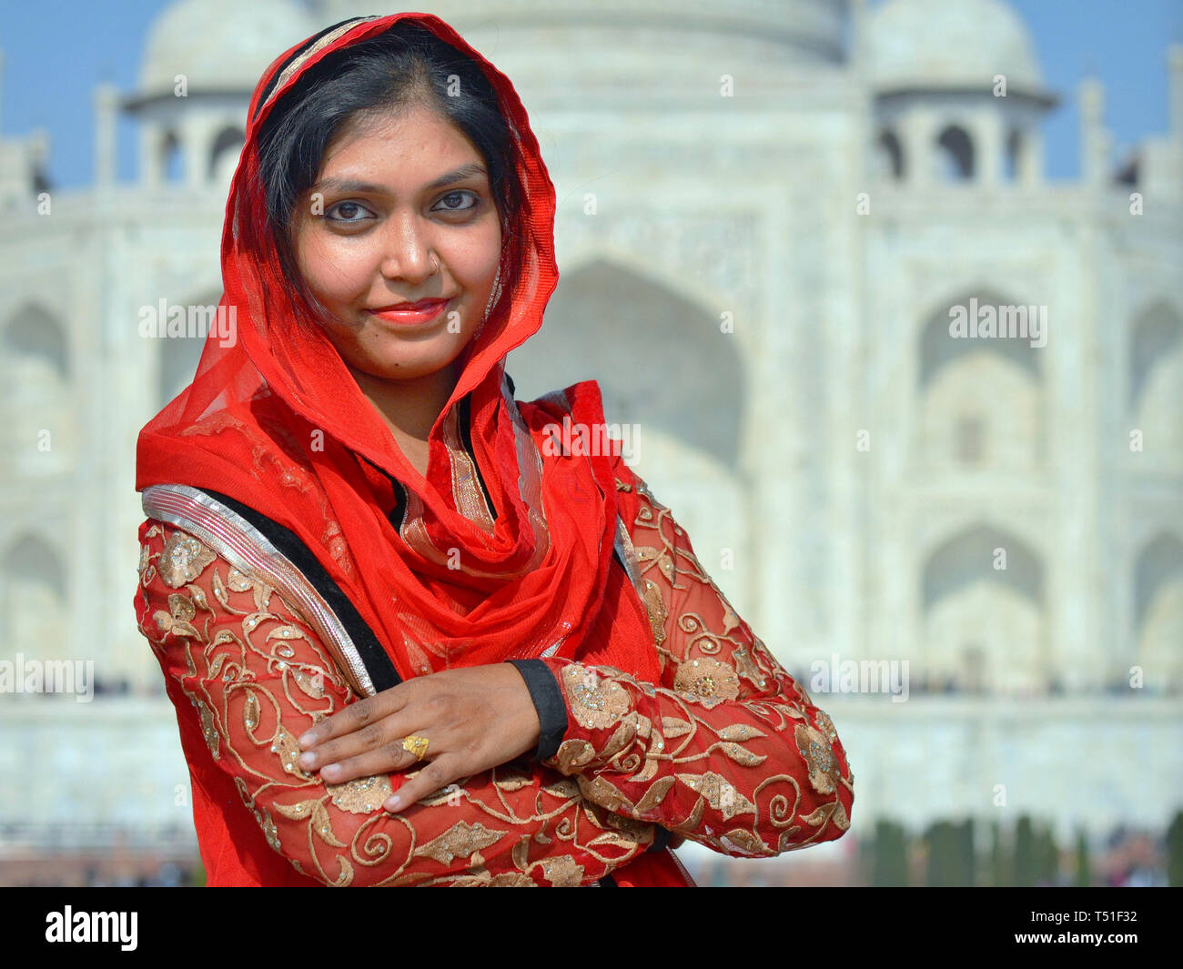 Belle jeune femme indienne en rouge pose devant le Taj Mahal. Banque D'Images