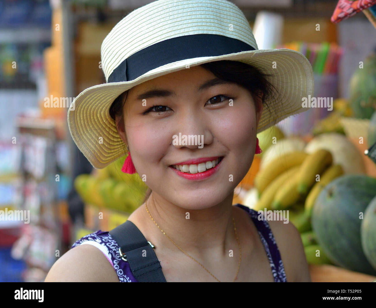 Jeune beauté asiatique avec un chapeau de paille démontre un sourire social (contrôlée ou "posés" [ou "faux"] sourire) ; image no. 1 de 2. Banque D'Images
