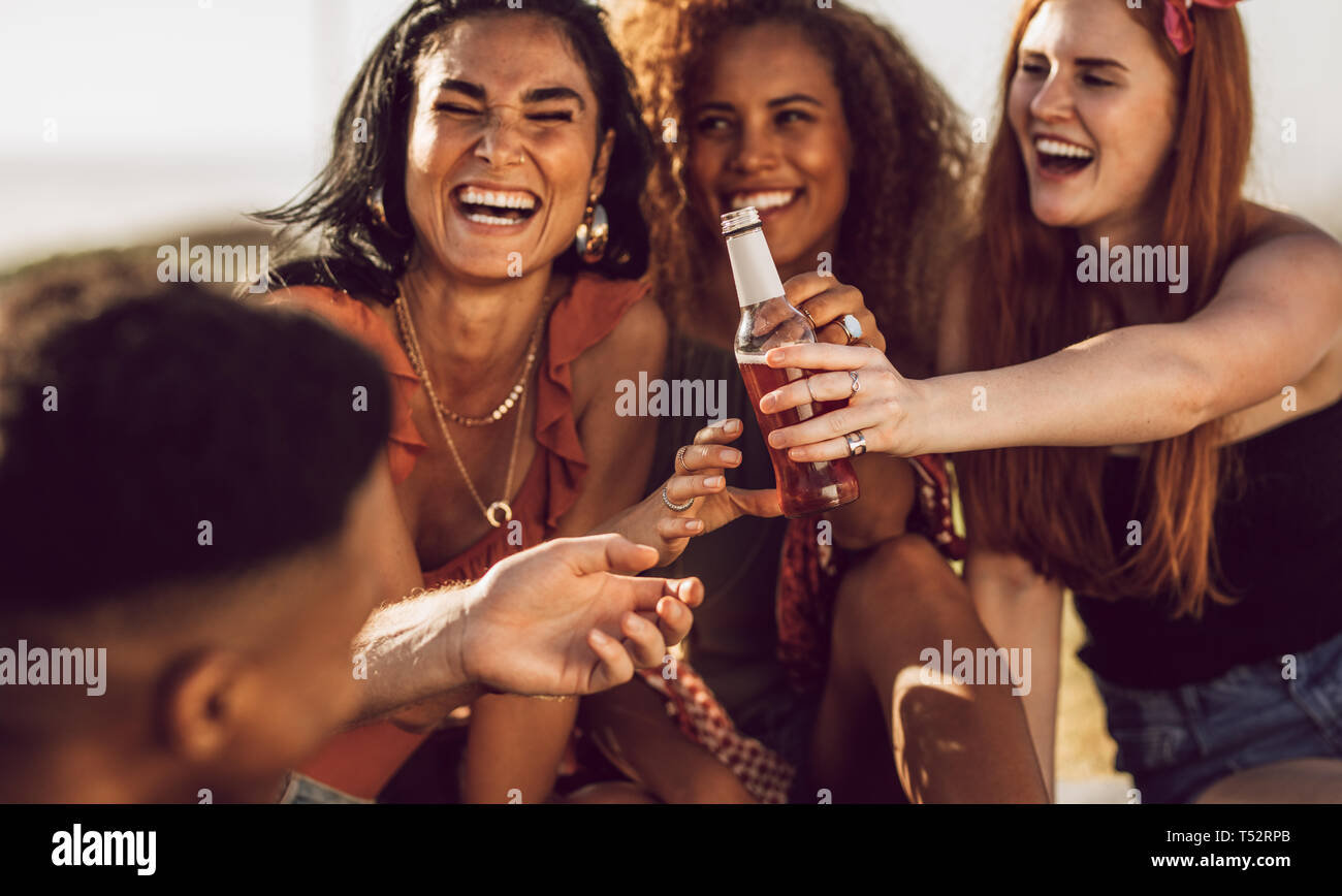 Les jeunes femmes donnant une bouteille de bière à un ami et de rire. Groupe diversifié de friends en plein air avec des bières. Banque D'Images