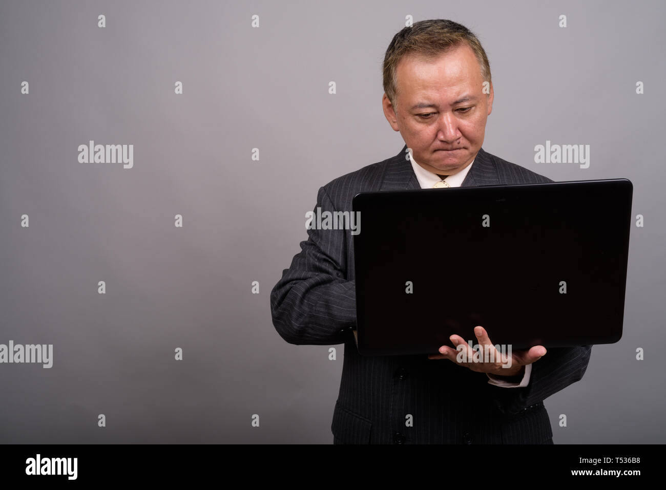 Portrait of mature Asian businessman contre l'arrière-plan gris Banque D'Images