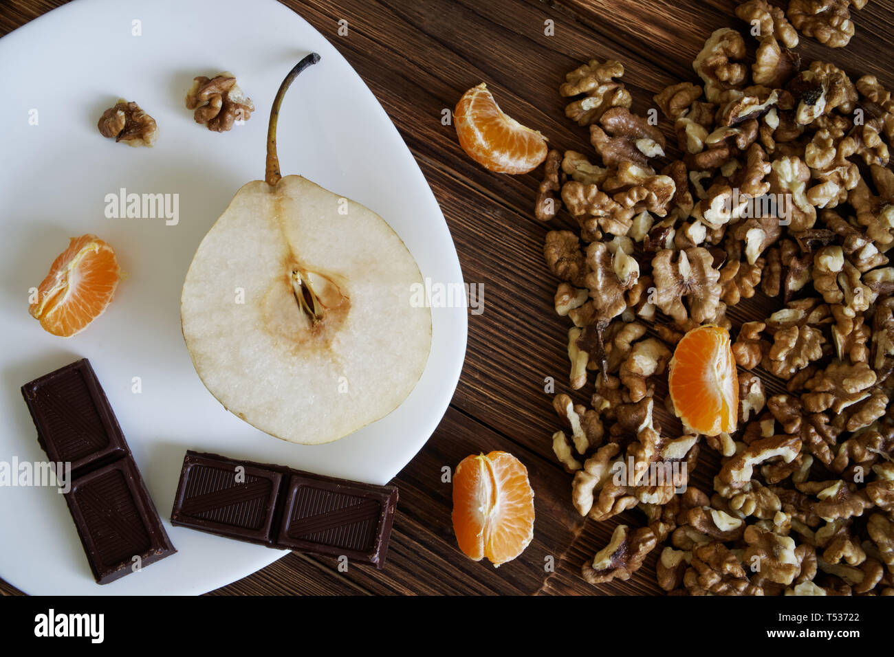 Noix pelées, la moitié des poires, chocolat et mandarines tranches dans une assiette blanche sur une surface en bois naturel de pin. La vie encore rustique. Banque D'Images