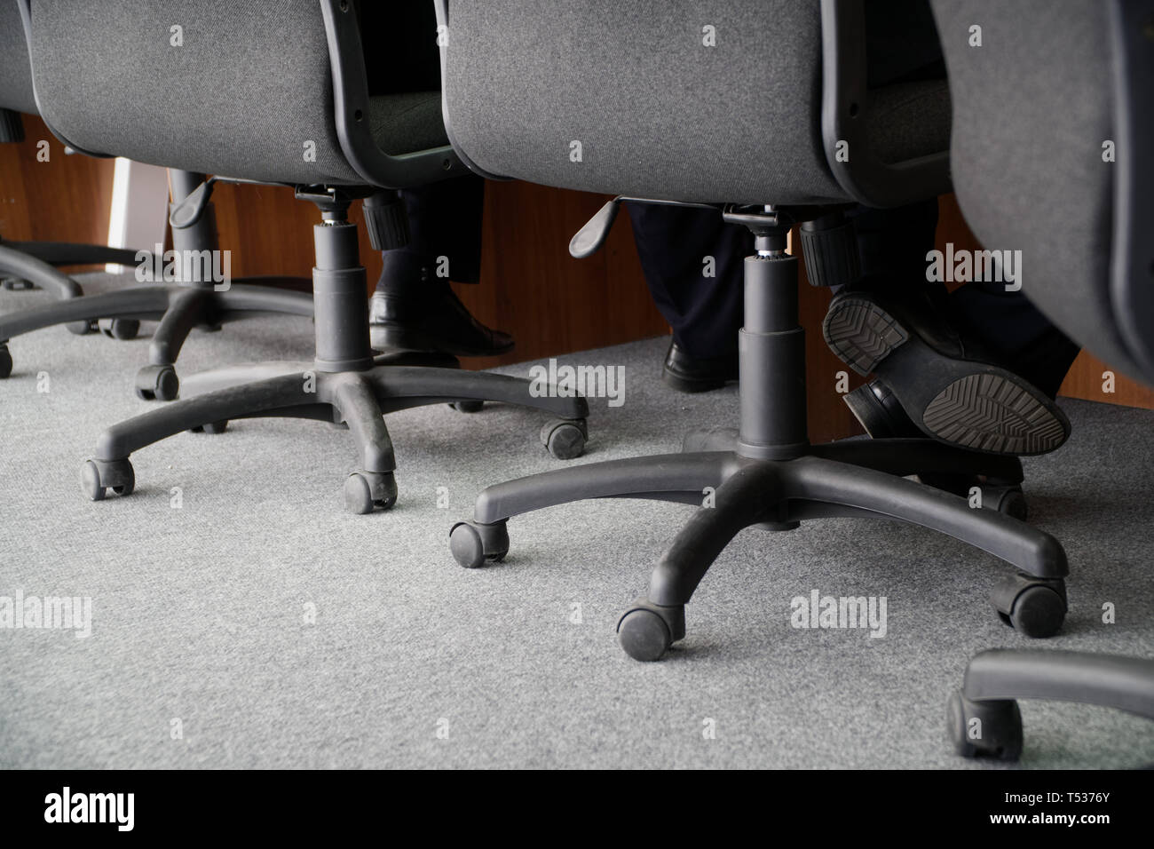 Chaises de bureau sur roues pour devoir au travail. Les jambes de deux hommes en service, assis dans des chaises. Tâches de bureau. Banque D'Images