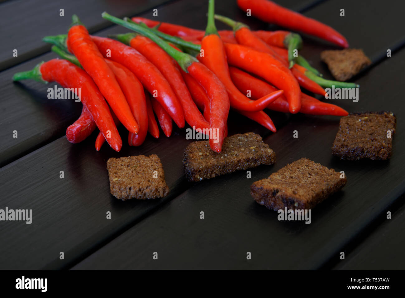 Les gousses de piment rouge et de croûtons de pain noir avec de l'ail se situent sur une table rustique en bois noir. Planches de pin peint surface. La lumière du jour. Libre. Banque D'Images