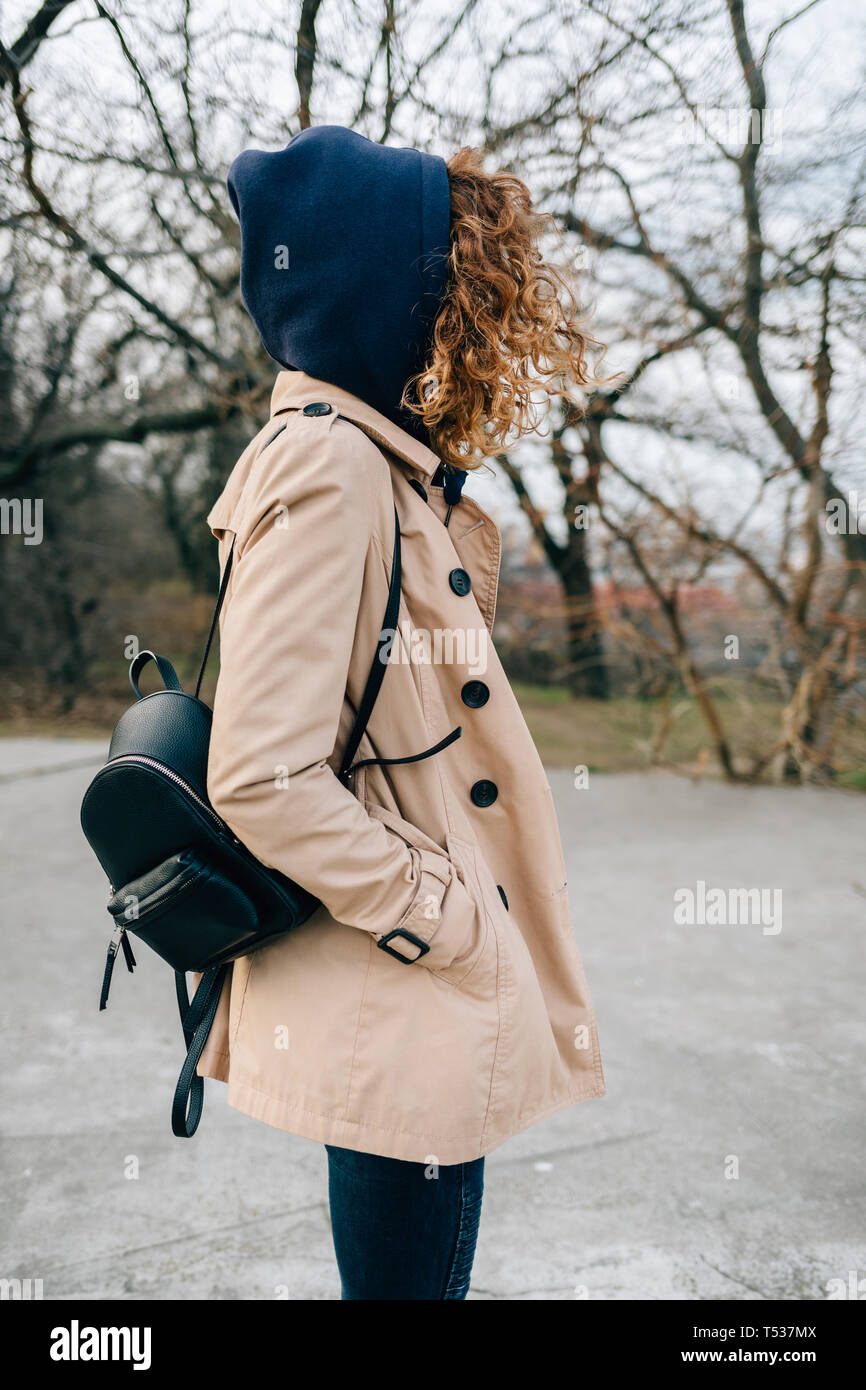 La mode élégante jeune femme vêtue de trench-coat beige et le capot noir  avec sac à dos debout dans city park holding hands in pockets, vi Photo  Stock - Alamy