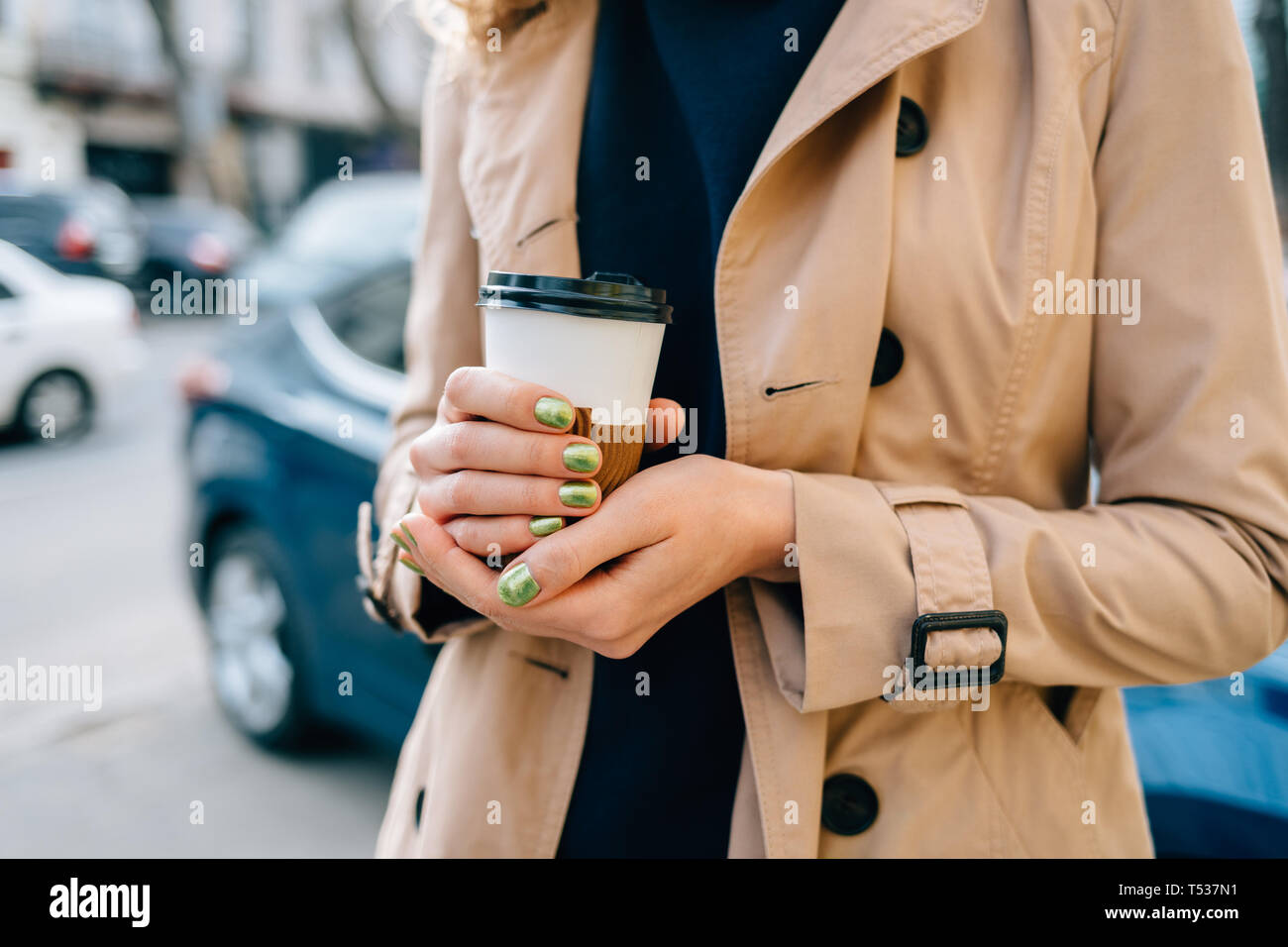 Close-up of young woman holding disposable cup de café chaud dans ses mains l'article on city street près de voiture et la route. Banque D'Images