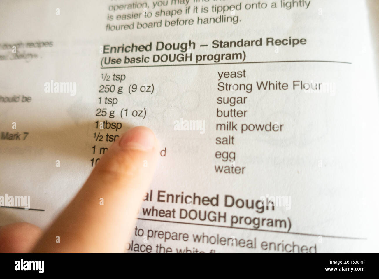 Un enfant suit recette dans un livre de cuisine et utilise ses doigts pour suivre les mots pendant qu'il lit. Banque D'Images