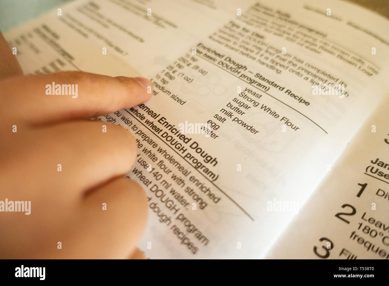 Un enfant suit recette dans un livre de cuisine et utilise ses doigts pour suivre les mots pendant qu'il lit. Banque D'Images