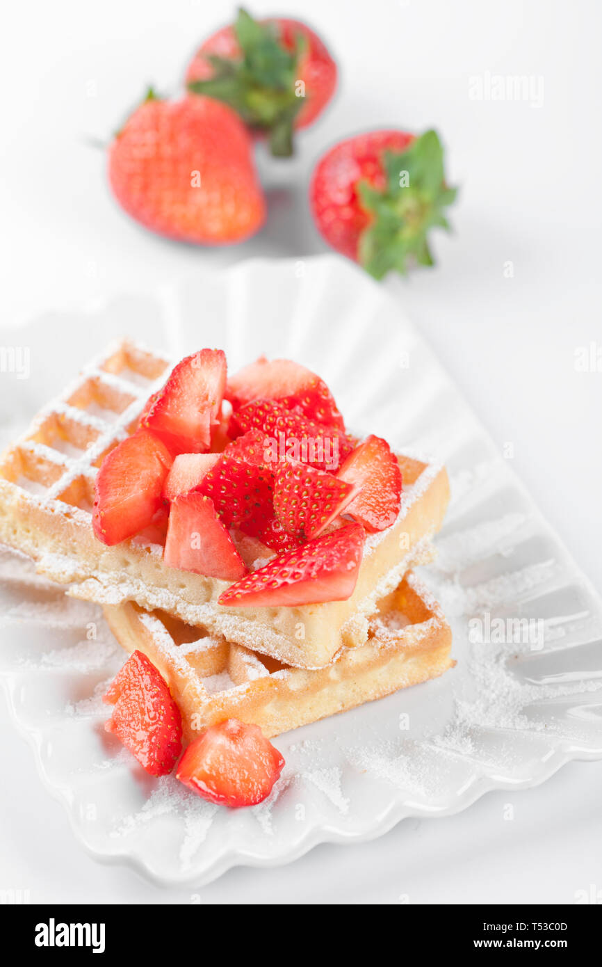 Belgique waffers avec du sucre en poudre et les fraises sur une plaque en céramique sur le tableau blanc. Des wafers. Banque D'Images