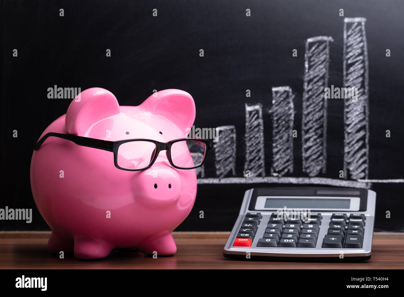 Close-up of Pink Piggybank and Calculator in front of Blackboard montrant Graphique Banque D'Images