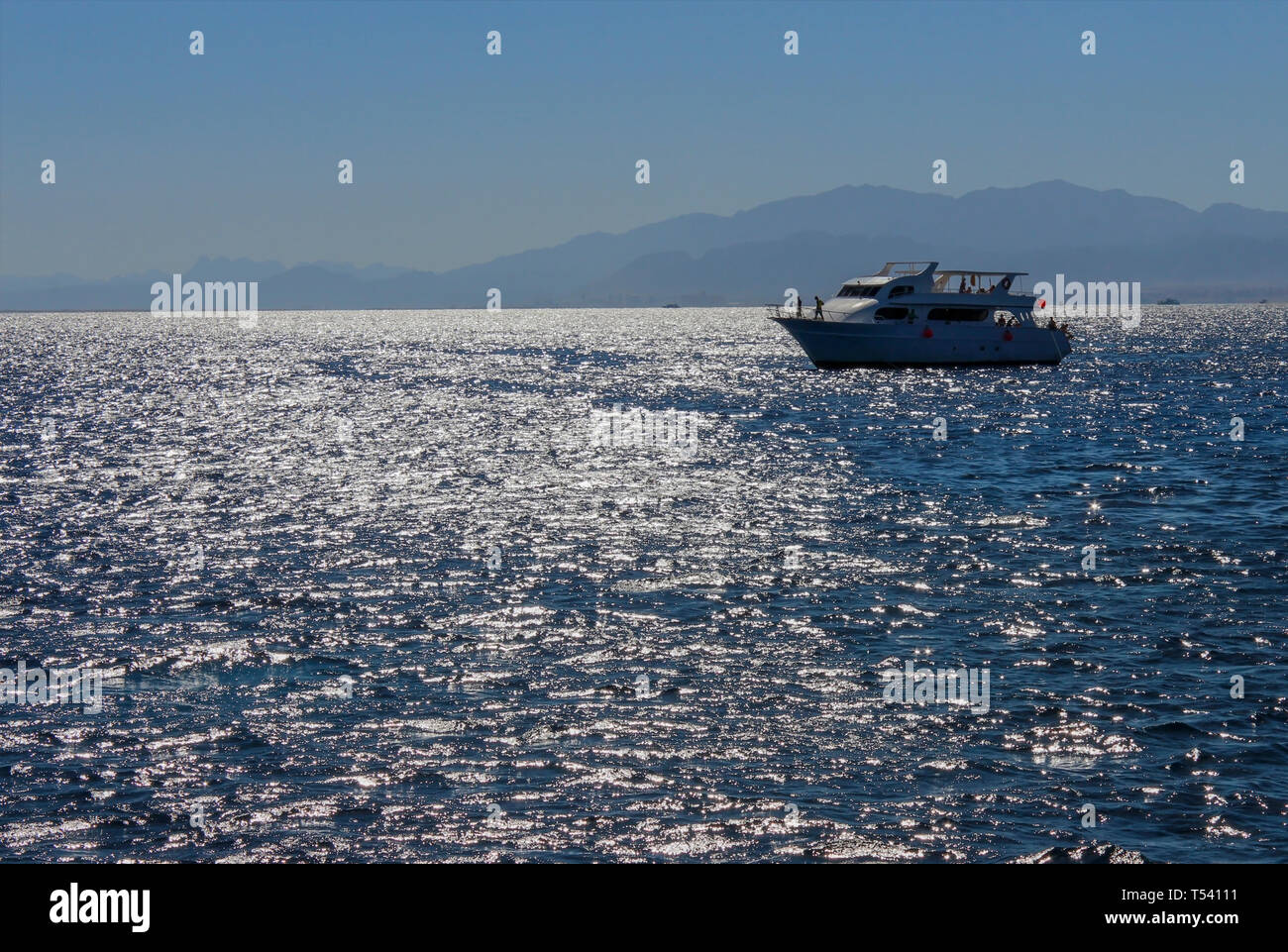 Paysage sur une journée ensoleillée avec vue sur la mer, sur un bateau et les montagnes au loin. Banque D'Images