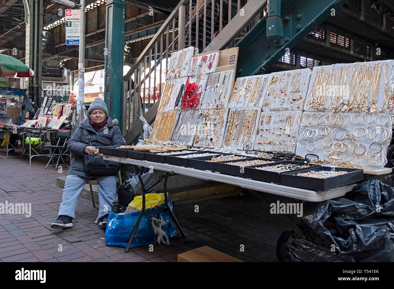 Une vieille femme d'Amérique du Sud la vente de bijoux pour les femmes à partir d'un se tenir sous l'élevé les wagons du métro . À Corona, Queens, NYC Banque D'Images