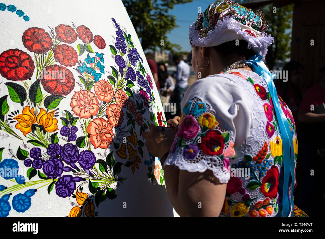 BUDAPEST/Hongrie - 04.21.2019 : un oeuf de Pâques géant blanc est décoré de motifs floraux folklore par une jeune femme portant Hungaria traditionnels Banque D'Images
