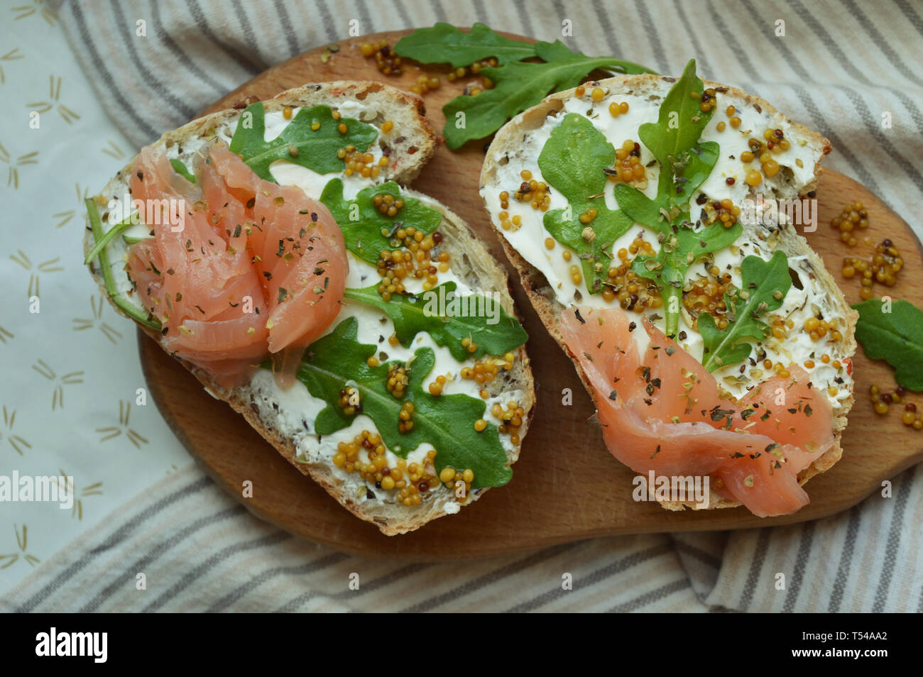 Des sandwiches au saumon avec du fromage à la crème, les graines de moutarde, l'huile d'olive, roquette sur pain de seigle grillé, servi sur la planche de bois. La mode en bonne santé l'alimentation. Banque D'Images