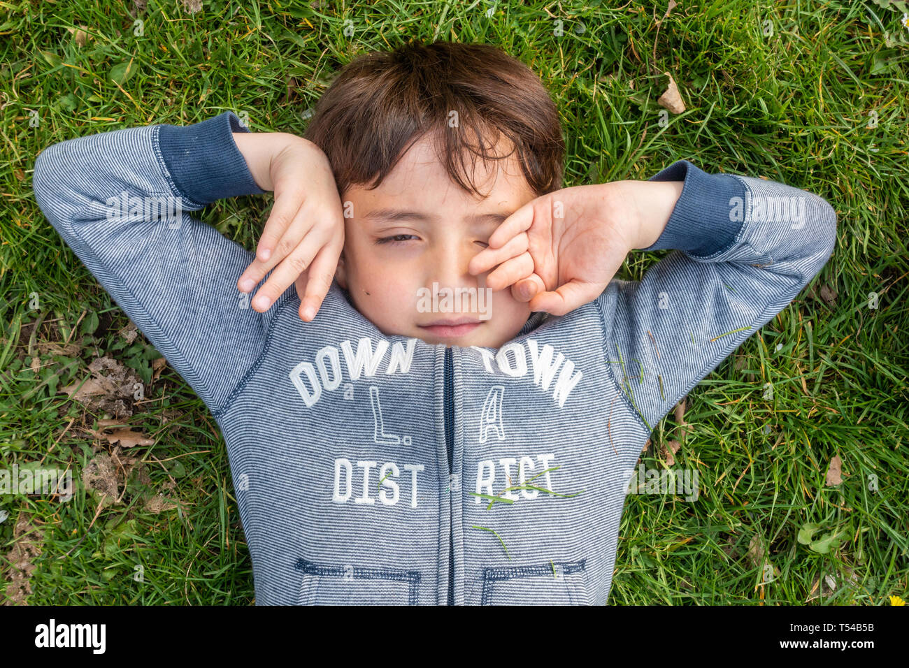 Un jeune garçon se couche sur l'herbe, et s'étend. Banque D'Images