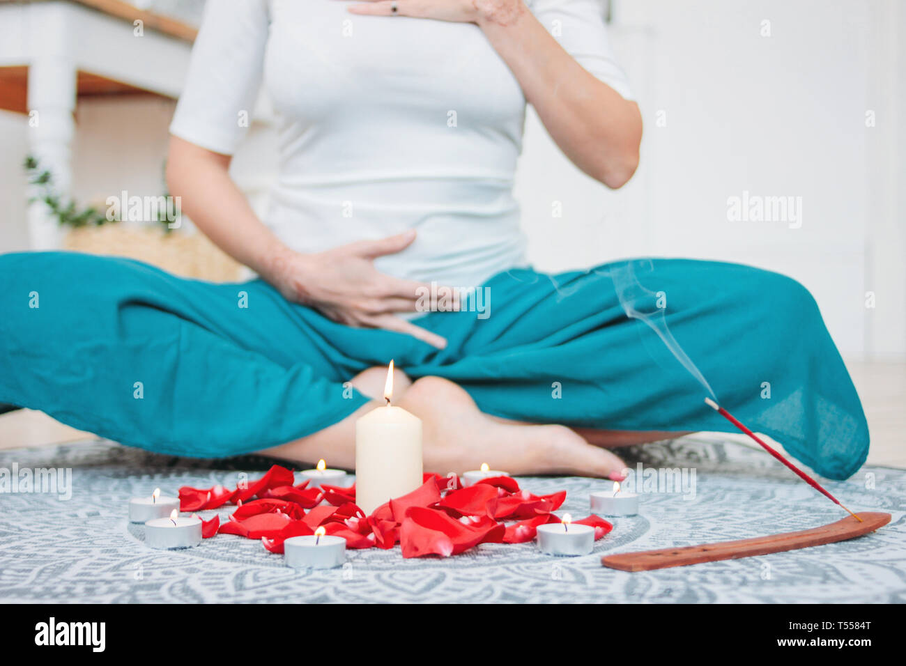 Femme en costume ethnique pratiquant le yoga en face de bougies et de pétales de rose rouge, avec les mains sur le chakra du cœur mehendi Banque D'Images