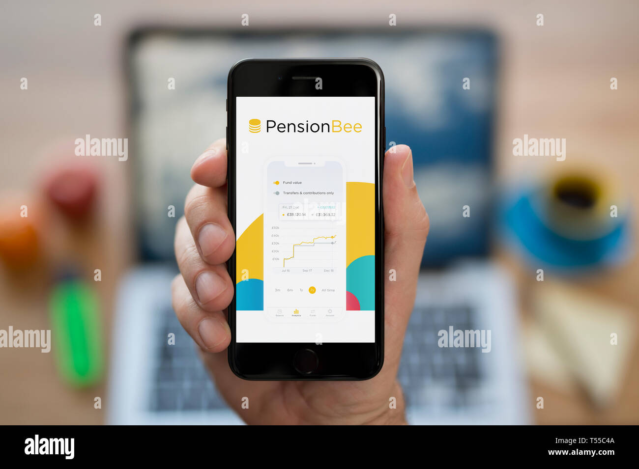 Un homme se penche sur son iPhone qui affiche le logo de l'abeille de pension (usage éditorial uniquement). Banque D'Images