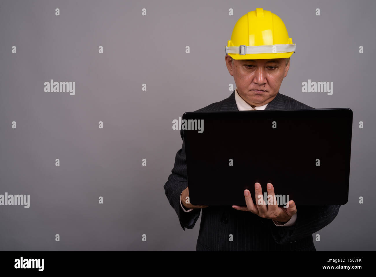 Mature Asian businessman construction contre l'arrière-plan gris Banque D'Images