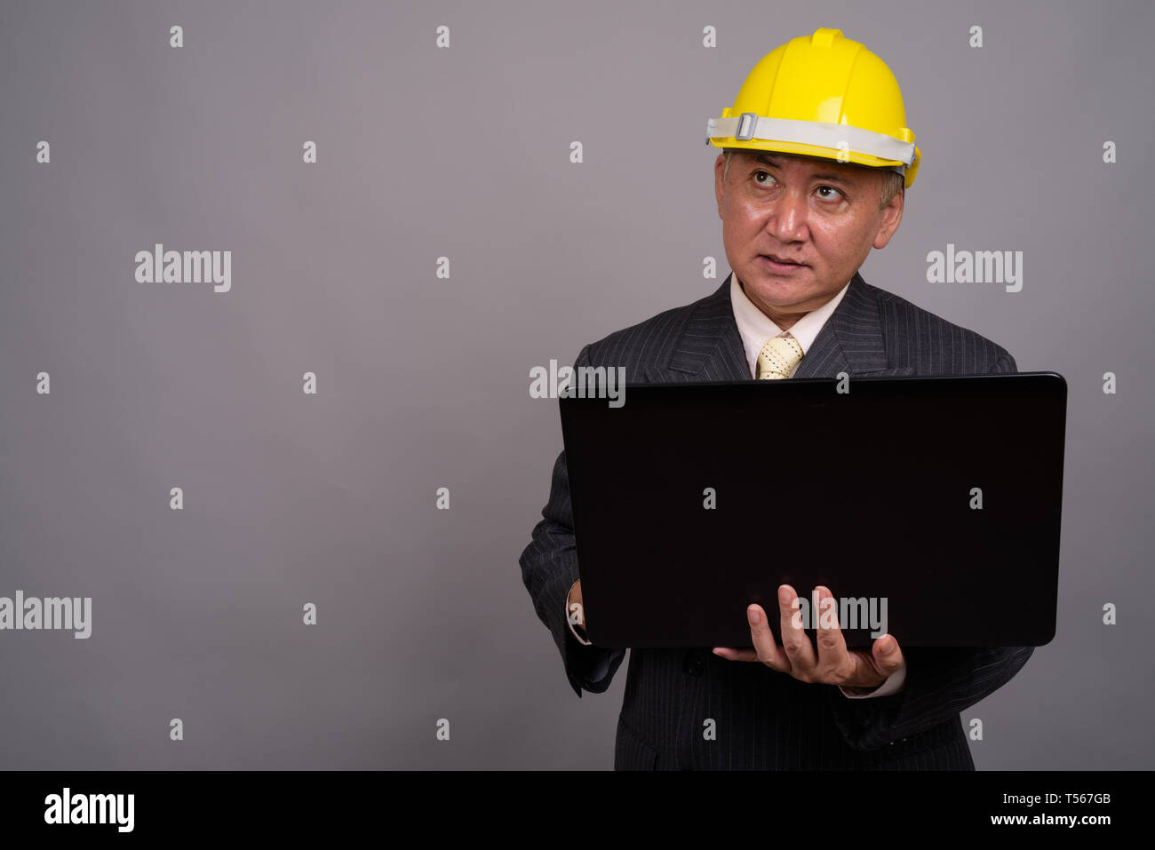 Mature Asian businessman construction contre l'arrière-plan gris Banque D'Images