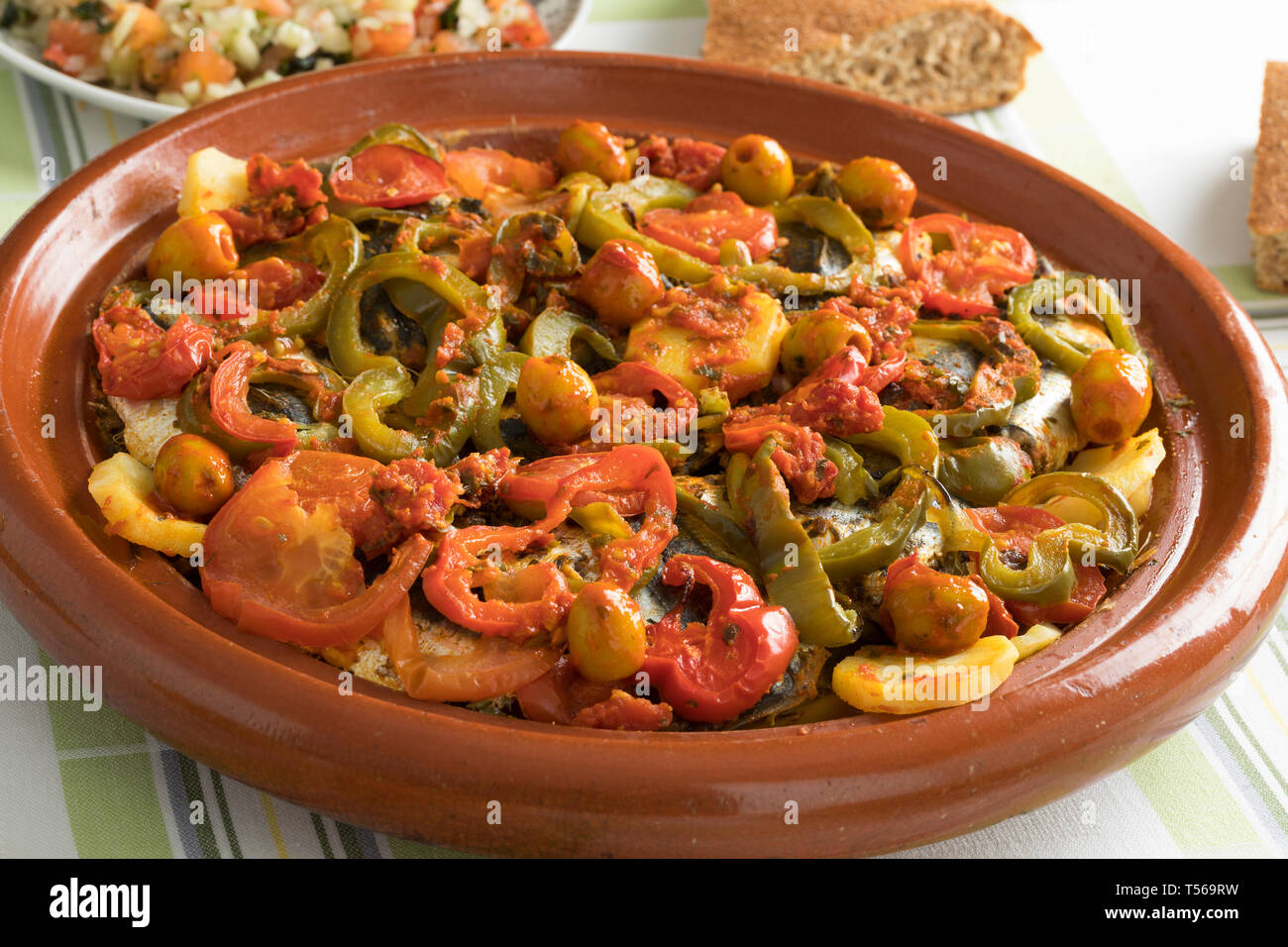 Tajine marocain traditionnel avec des sardines, des légumes et du pain sur la table pour le dîner Banque D'Images